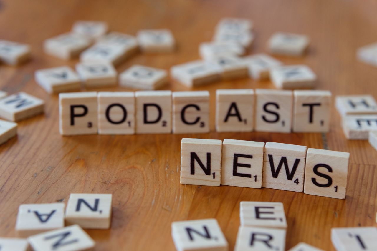 Wooden letter tiles spelling out PODCAST NEWS on a wooden surface.